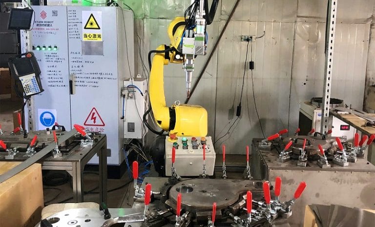 Yellow robotic arm performing precision laser welding in an automated manufacturing setup